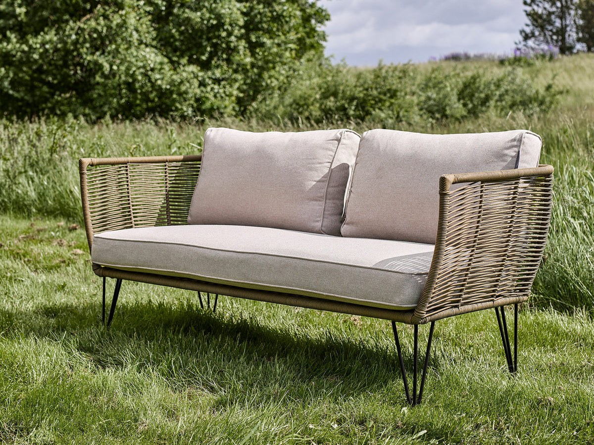Lounge Sofa Mundo von Bloomingville in Grün mit Flechtoptik, schwarzem Eisengestell und hellen Kissen, als Aussenmöbel für Terrasse und Garten.