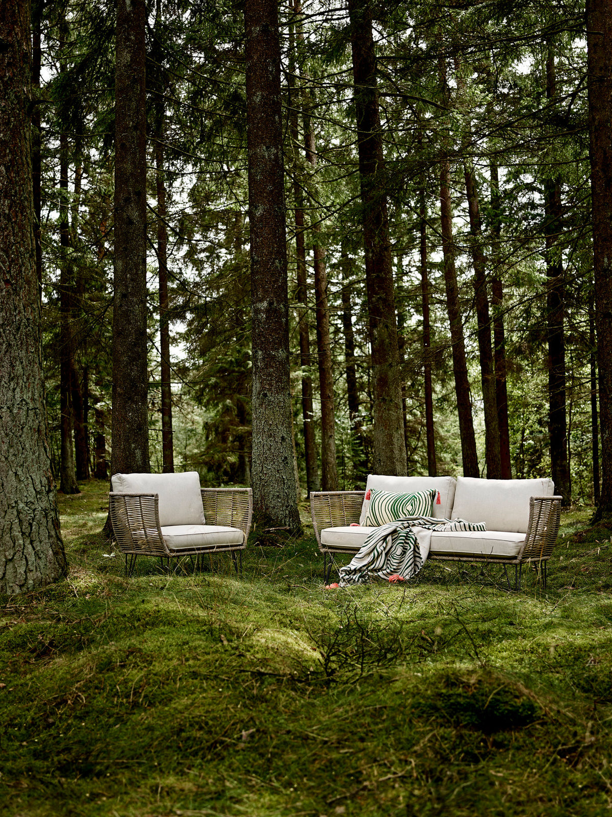Braunes Lounge Sofa mit Flechtoptik, schwarzem Eisengestell und hellen Kissen, Modell Mundo von Bloomingville im Aussenbereich.
