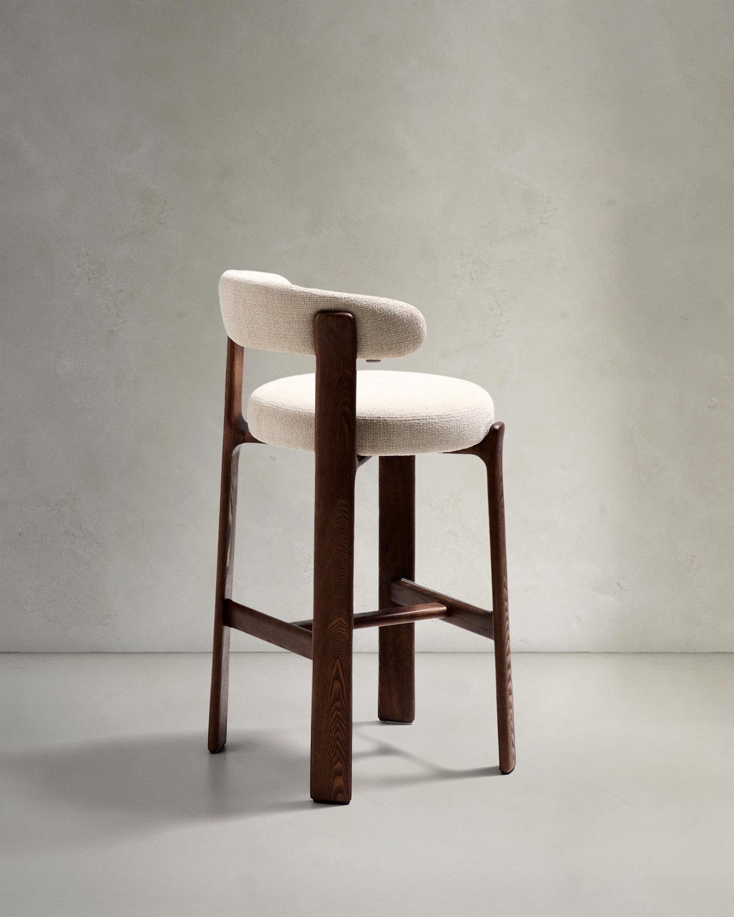 Erleben Sie den Hocker Granite von Kave Home: Beigefarbene Chenille und massives Eschenholz vereinen sich in einem stilvollen, skandinavischen Design.