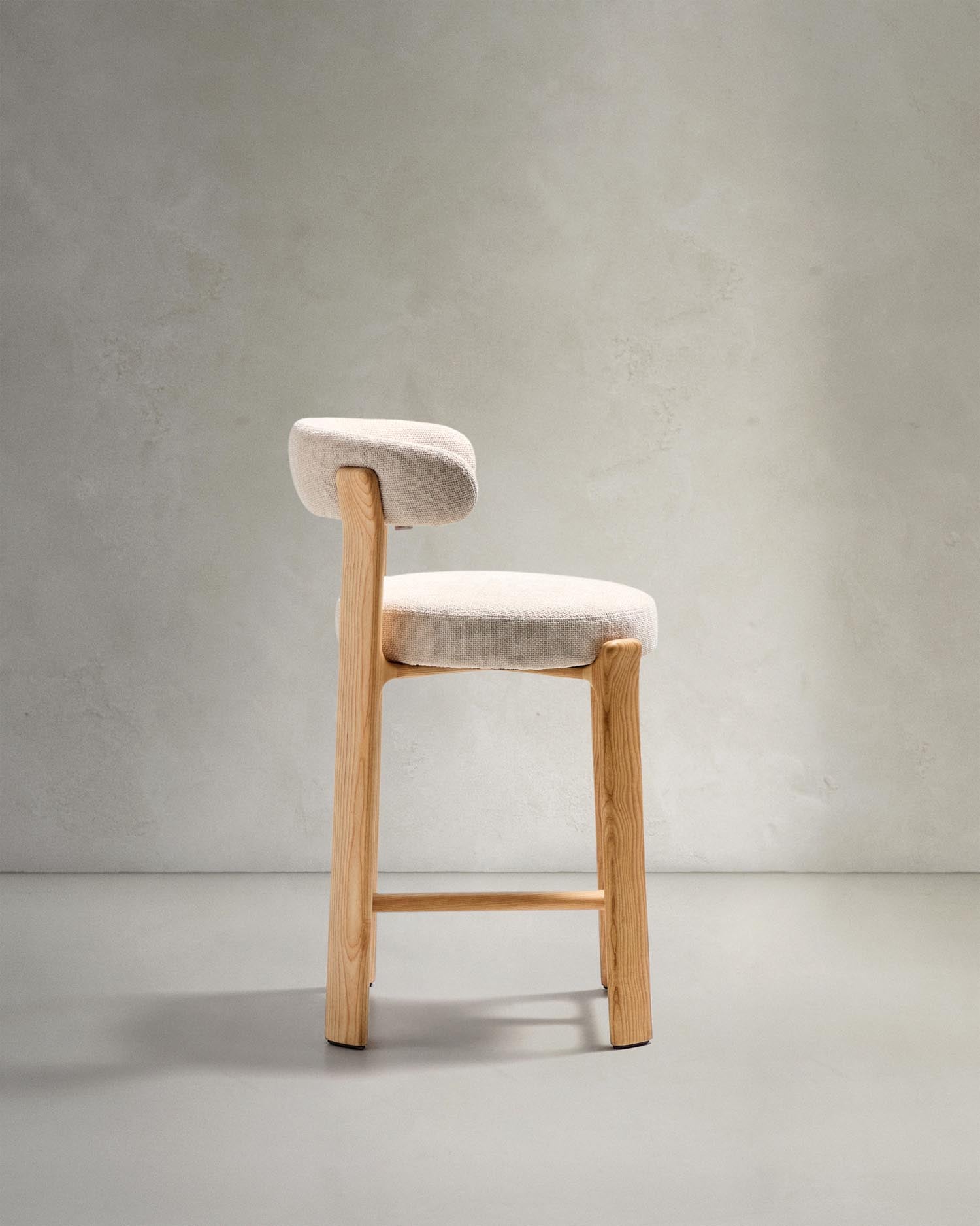 Entdecken Sie den Hocker Granite von Kave Home: Beigefarbene Chenille und massives Eschenholz vereinen sich in stilvollem skandinavischen Design.