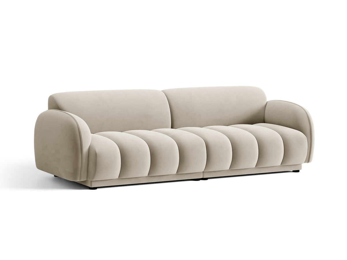 Vierersofa Bilbao mit hellbeigem Samtbezug, schwarzen Kunststoffbeinen und klarer, gerader Linienführung, fotografiert freistehend im Raum.