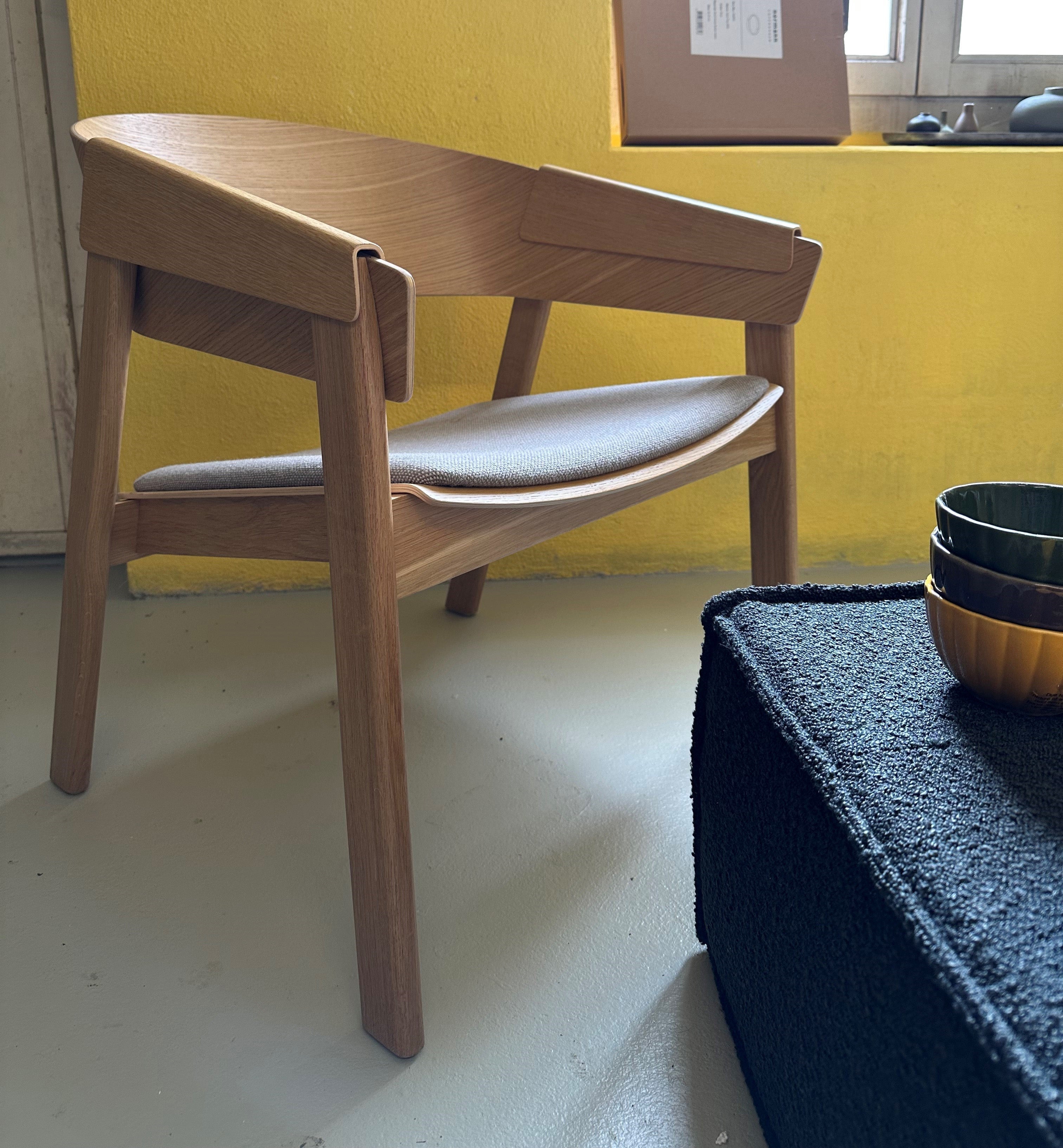 Ein moderner Loungesessel aus Holz mit klaren Linien, sanft geschwungenen Armlehnen und einer zeitlosen, skandinavischen Ästhetik.