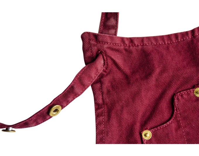 Kochschürze in Aubergine und Braun aus Canvas mit Rundhalsausschnitt, schmalen Seitenteilen, fünf Taschen und Knöpfen zur Anpassung.