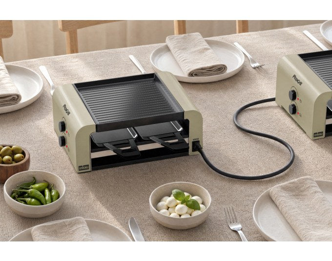 STÖCKLI Tischgrill PizzaGrill 4 Connect in Ivory Gold mit wendbarer Aluguss-Grillplatte, vier Pfännchen und Kunststoffspachteln auf dem Esstisch.