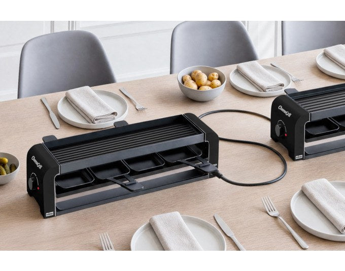 Schwarzer STÖCKLI Tischgrill CheeseGrill 4 Connect mit wendbarer Grillplatte, vier Pfännchen und Kunststoffspachtel auf hellem Untergrund.