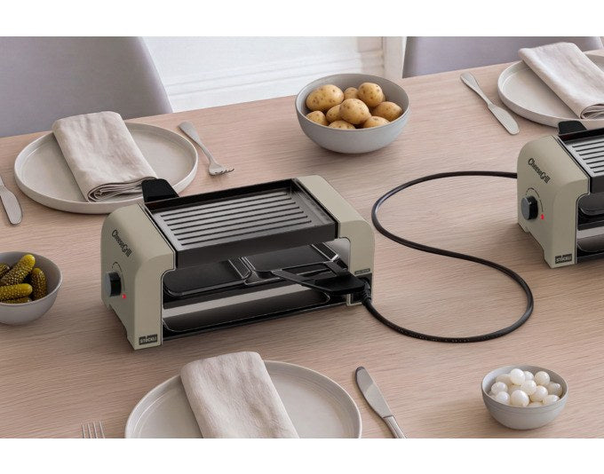 Tischgrill STÖCKLI CheeseGrill 2 Connect in Ivory Gold mit zwei Pfännchen, Wende-Grillplatte und Parkdeck auf hellem Hintergrund.