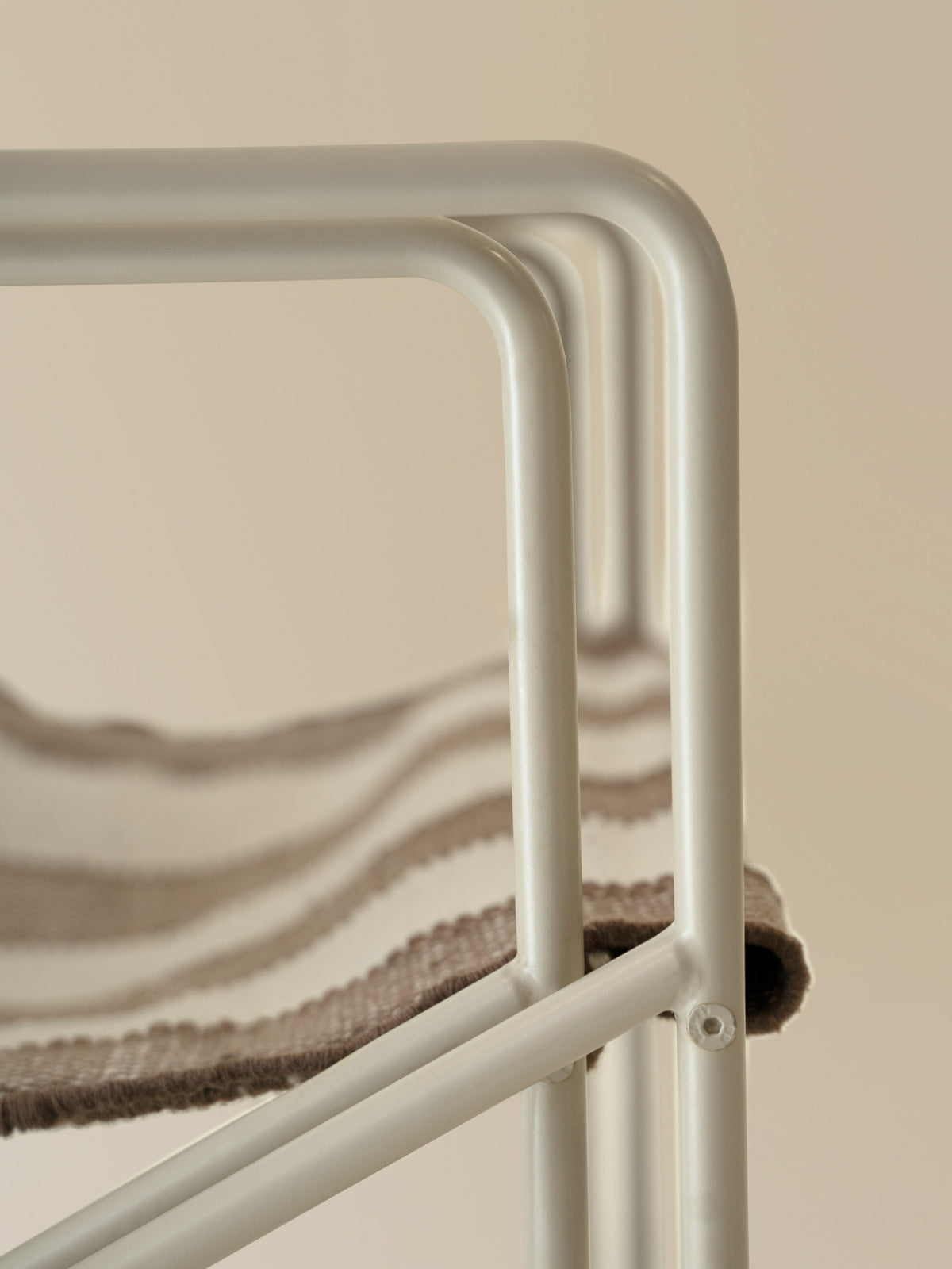 Desert Loungestuhl von Ferm Living: Outdoor-Sessel mit Armlehnen, röhrenförmigem Stahlgestell und handgewebtem Sitz aus PET-Garn in Cashmere/Offwhite/Chocolate.
