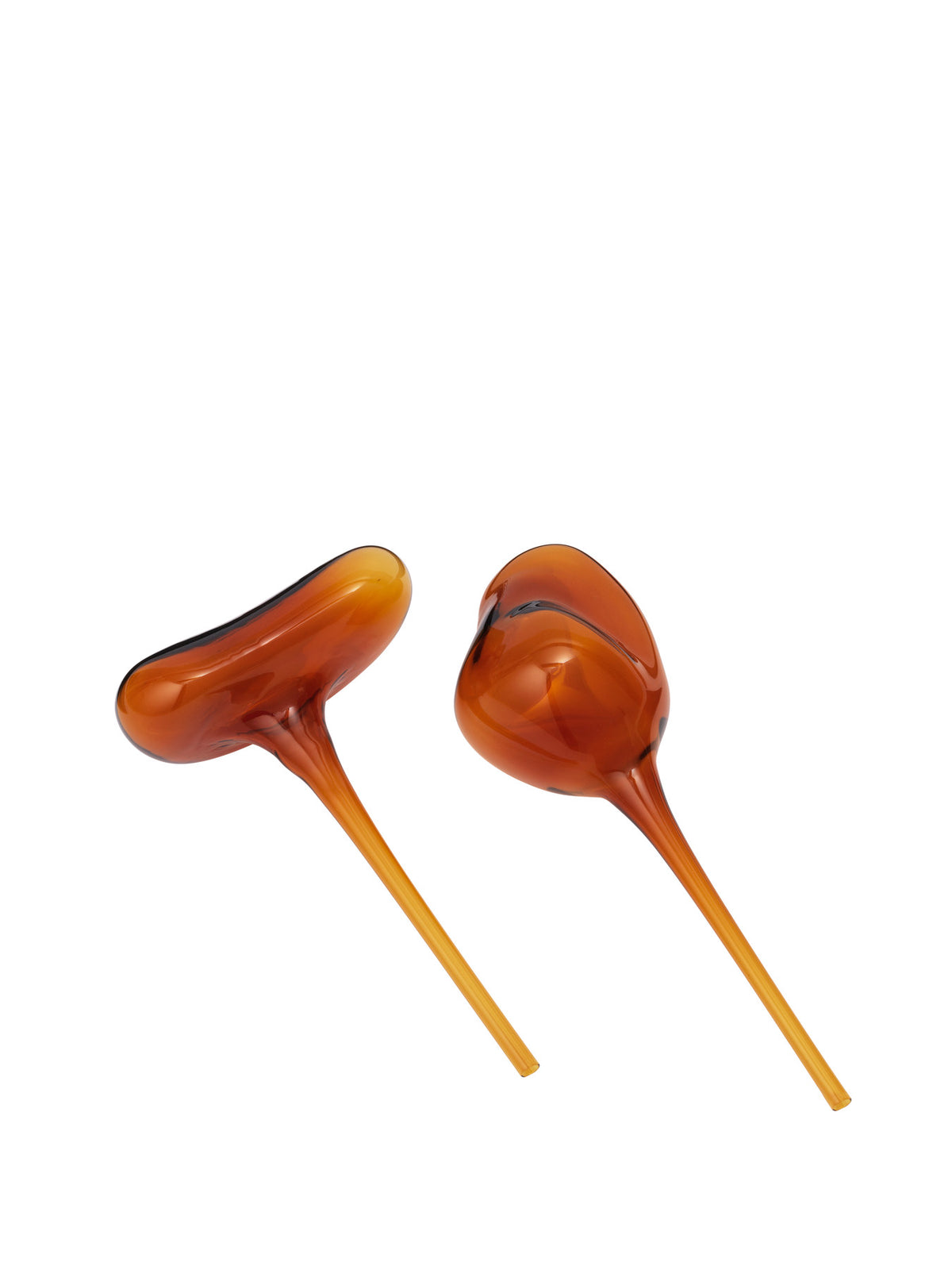 Zwei Wasserkugeln aus mundgeblasenem Glas in Amber von Ferm Living, organische Kugelform mit langem Stiel, stehend neben einem Pflanzentopf.