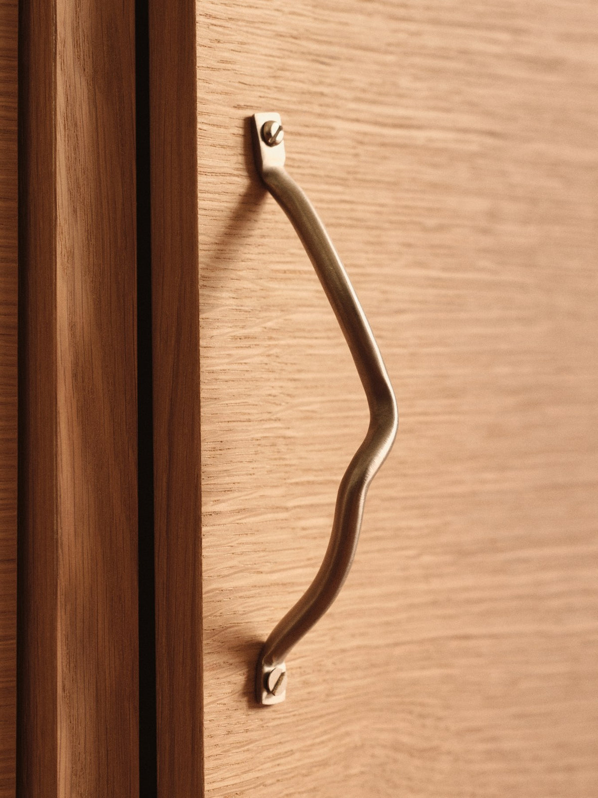 Curvature Handgriff von Ferm Living aus Edelstahl mit organisch geschwungener Form, montiert an einer Schrank- oder Schubladenfront.