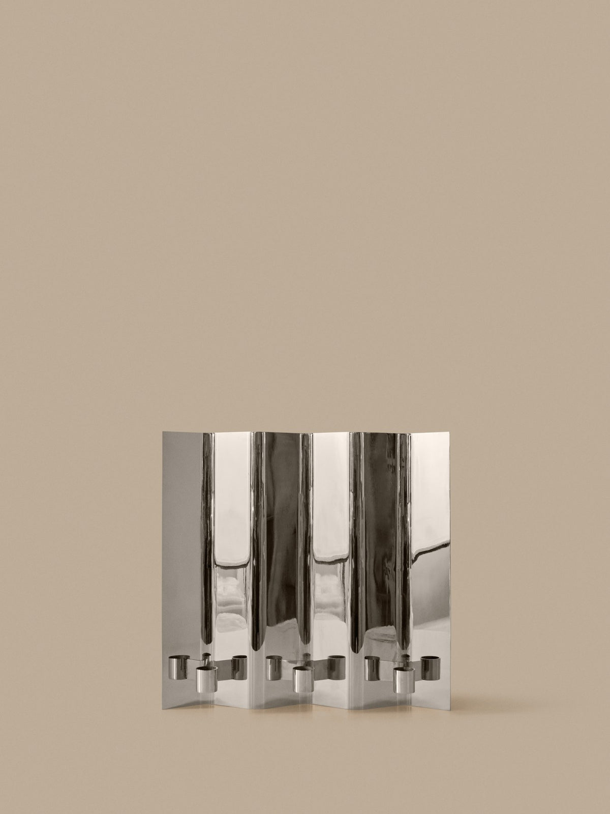 Wandkerzenhalter Eddy 3 von Ferm Living aus spiegelpoliertem Edelstahl, gefaltete Form für drei Kerzen, montiert an weisser Wand.