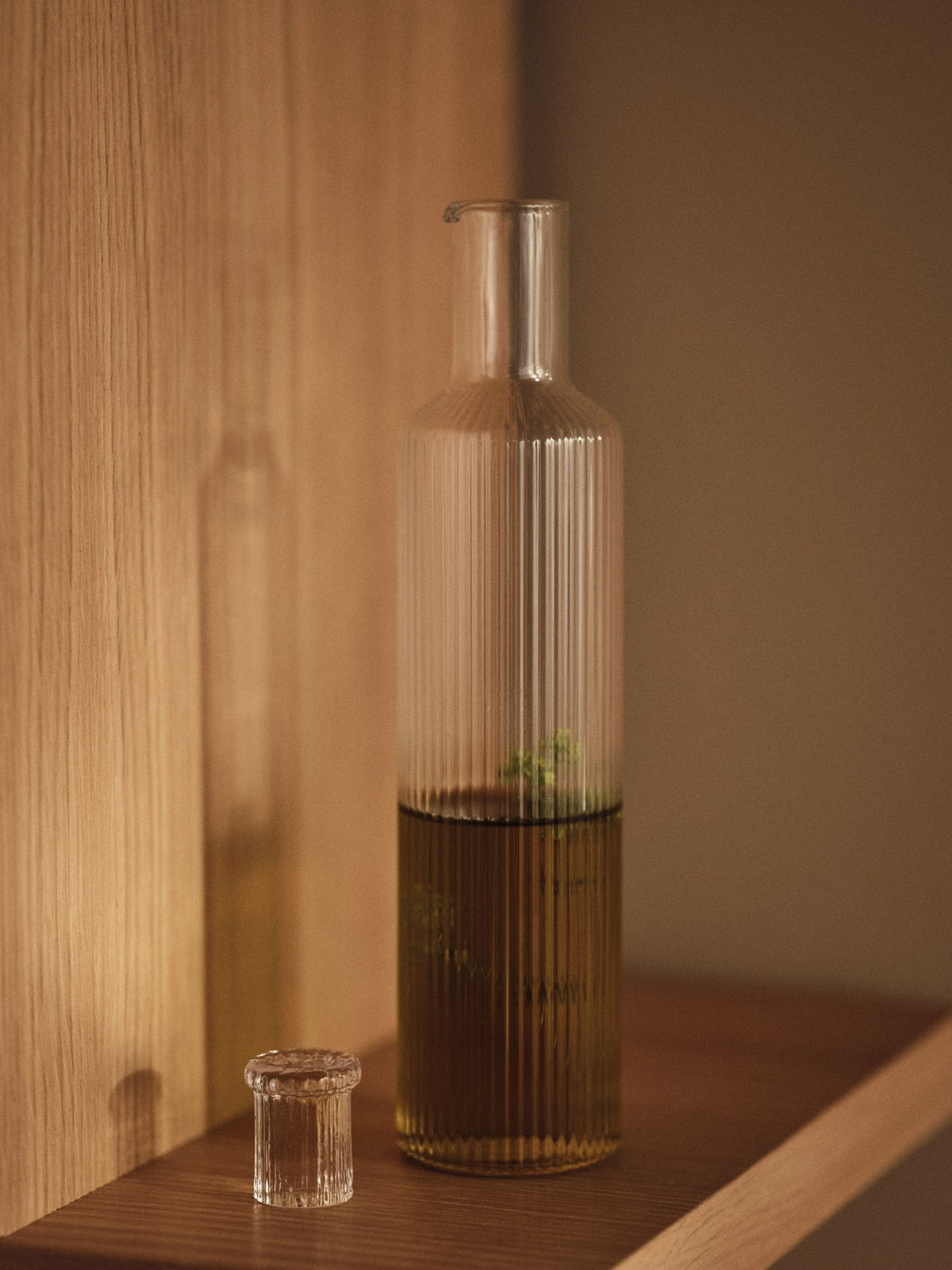Klare, mundgeblasene Glasflasche mit geriffelter Oberfläche und geometrischer Form, schlanker Hals mit Deckel, aus der Ripple-Serie von Ferm Living.