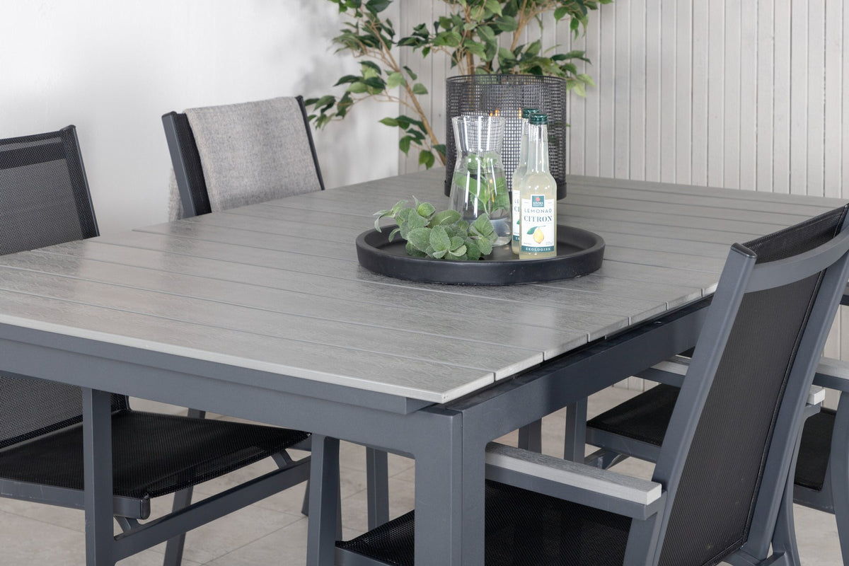 Rechteckiger Esstisch aus Aintwood mit Aluminiumgestell in Anthrazit, dazu zwei stapelbare Stühle mit pulverbeschichteter Oberfläche.