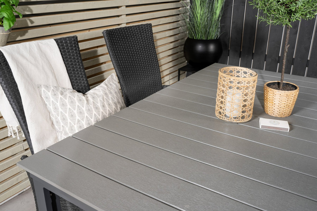 Foto eines rechteckigen Esstischs mit grauer Aintwood-Tischplatte und Aluminiumbeinen sowie zwei schwarzen Relaxsesseln mit Polyesterbezug im Garten.