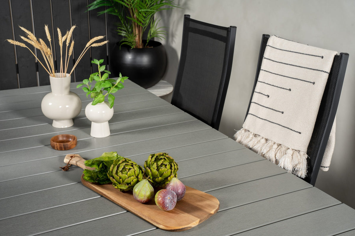 Rechteckiger Gartentisch mit grauer Aintwood-Platte und Aluminiumgestell, daneben zwei stapelbare Copacabana-Relaxsessel in Schwarz.