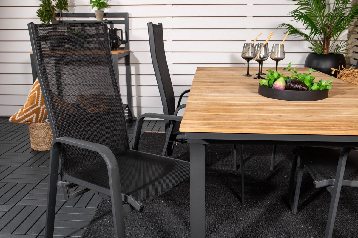 Zwei schwarze Relaxsessel Copacabana aus Aluminium mit Pulverbeschichtung neben rechteckigem Teak-Esstisch Mexico in Natur, Gartenmöbel-Set.