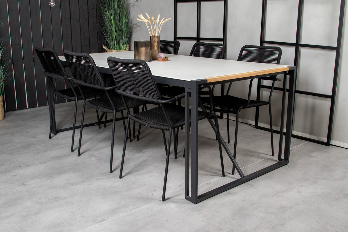 Zwei schwarze Esszimmerstühle mit geflochtener Seilsitzfläche und Aluminiumgestell neben rechteckigem Esstisch mit Glas-Teak-Platte und Stahlbeinen.
