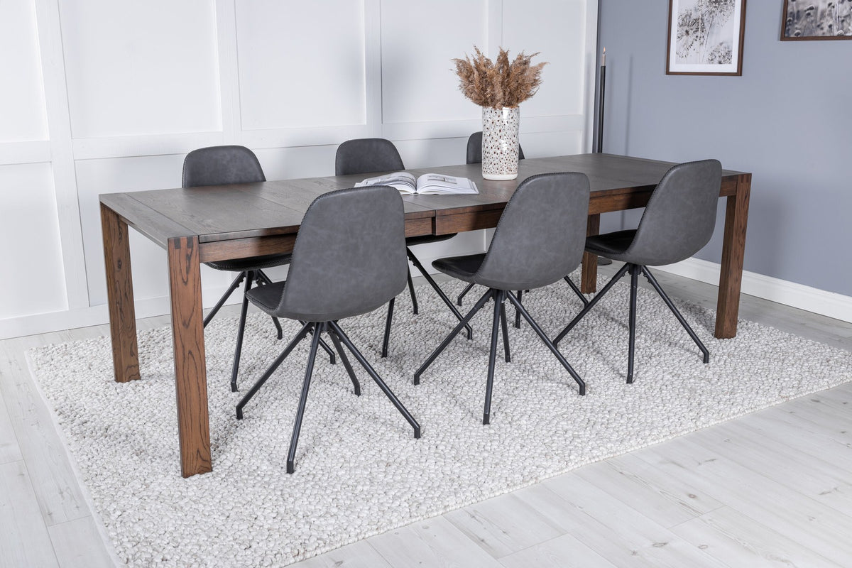 Rechteckiger Esstisch aus Eiche in Natur mit ausziehbarer Platte, dazu zwei schwarze Esszimmerstühle mit gepolsterter Sitzfläche von Venture Home.
