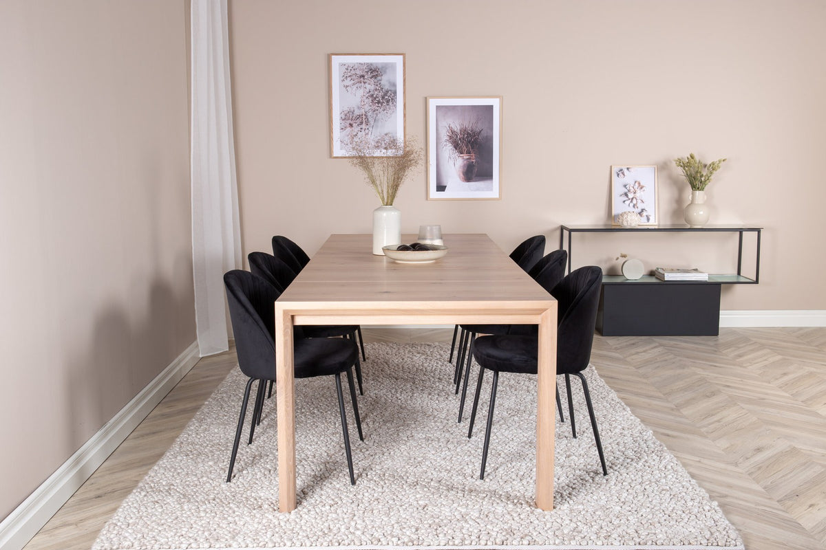 Rechteckiger Esstisch aus Eiche mit weissgelaugter Tischplatte, kombiniert mit zwei schwarzen Esszimmerstühlen im skandinavischen Design.