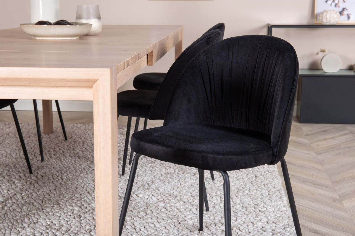 Rechteckiger Esstisch aus Eiche mit weissgelaugter Tischplatte, kombiniert mit zwei schwarzen Esszimmerstühlen im skandinavischen Design.
