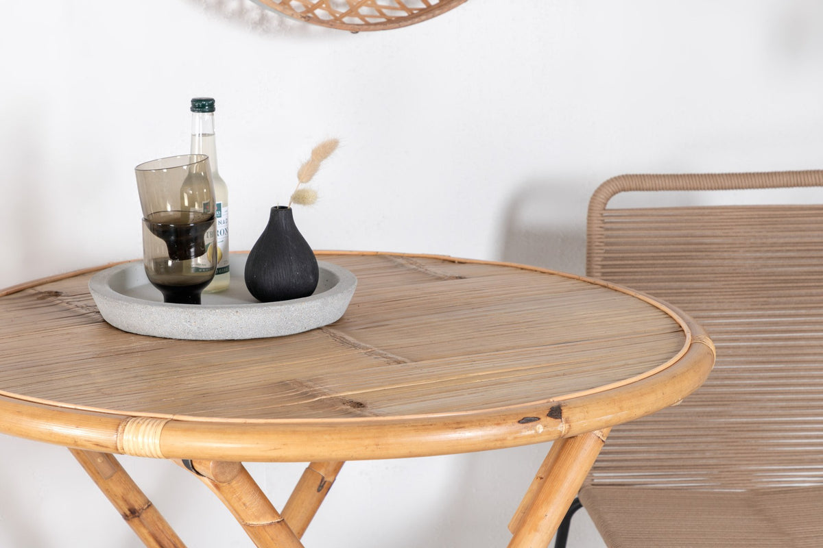 Runder Cafétisch aus Bambus mit Stahlbeinen in Natur, daneben zwei stapelbare Stühle aus Bambus und Rattan in Braun, Gartentischset.