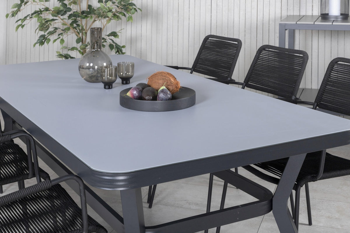 Rechteckiger Esstisch mit schwarzer Glasplatte und Stahlbeinen, daneben zwei schwarze Stühle mit Textilene-Bezug, Gartenmöbel-Set von Venture Home.