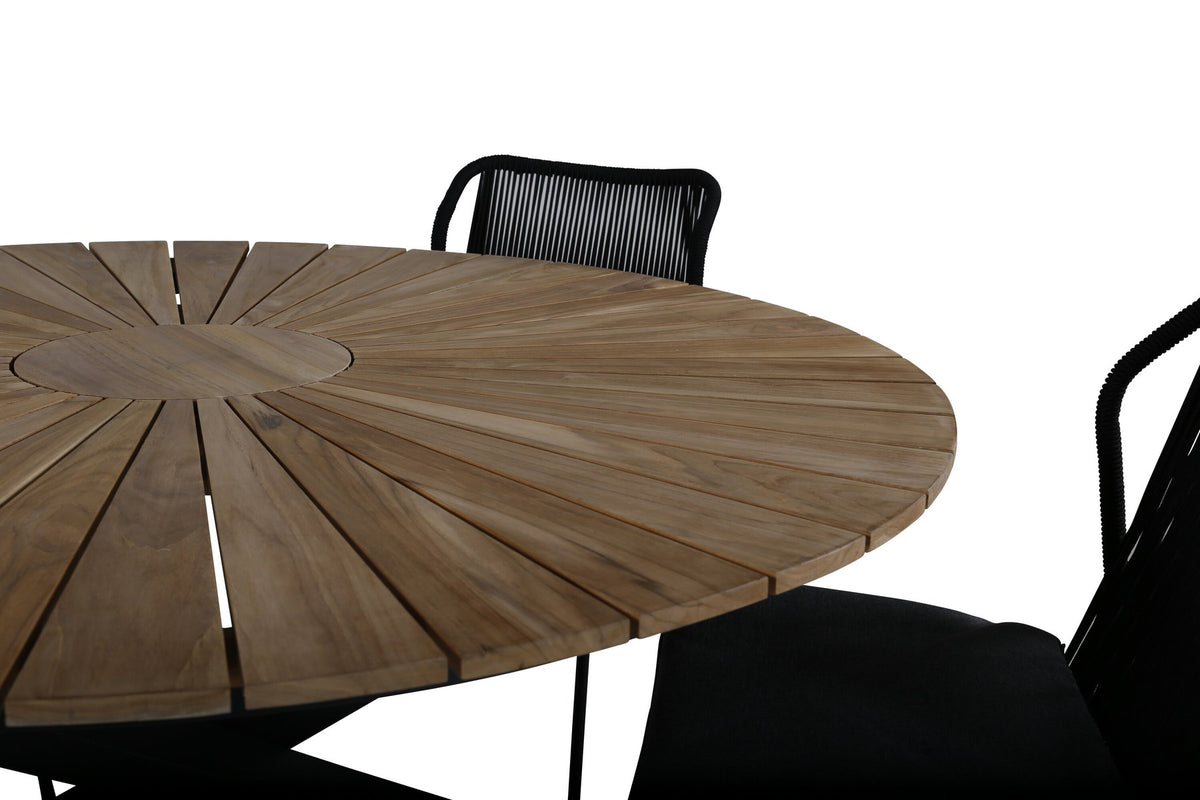 Vier schwarze Esszimmerstühle mit Aluminiumgestell und Polyesterbezug neben rundem Teak-Esstisch mit Stahlbeinen, Durchmesser 140 cm.