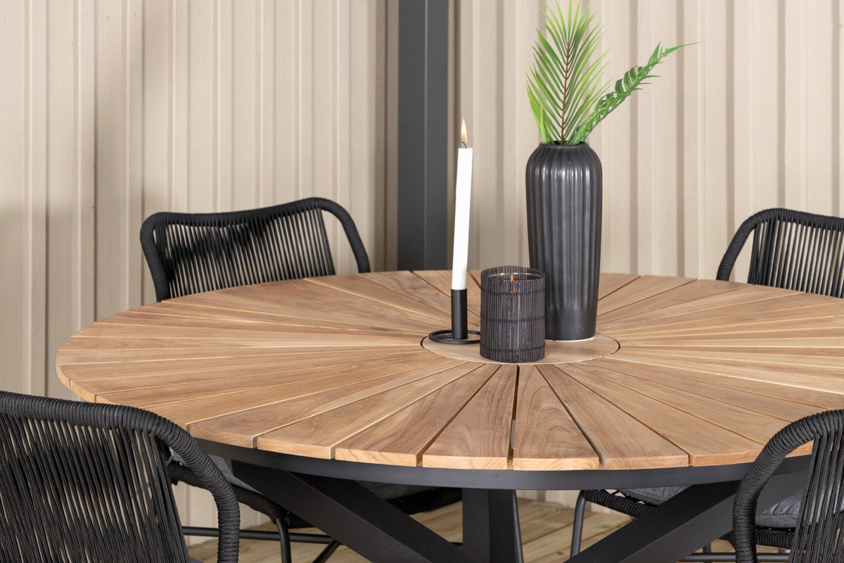 Vier schwarze Esszimmerstühle mit Aluminiumgestell und Polyesterbezug neben rundem Teak-Esstisch mit Stahlbeinen, Durchmesser 140 cm.