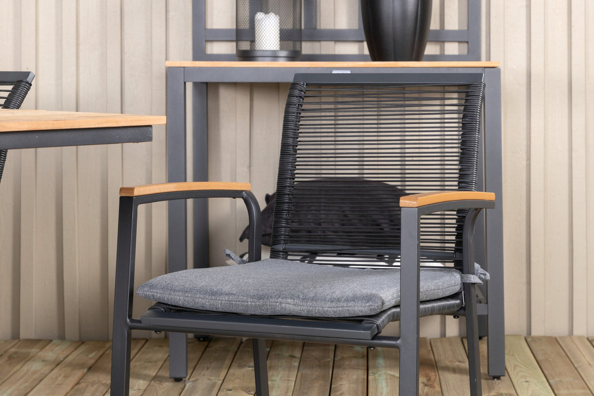 Foto eines schwarzen 2er-Stuhlsets mit Aluminiumgestell und Polyesterbezug neben einem rechteckigen Teak-Esstisch in Natur mit Stahlbeinen.