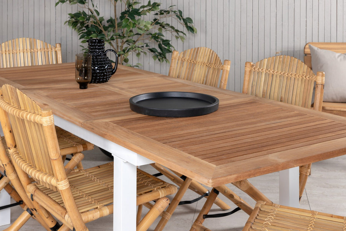 Foto zeigt einen Cafe Stuhl mit Rattan-Beinen und Stoffbezug in Natur sowie einen rechteckigen Teakholz-Esstisch mit weissem Aluminiumgestell.