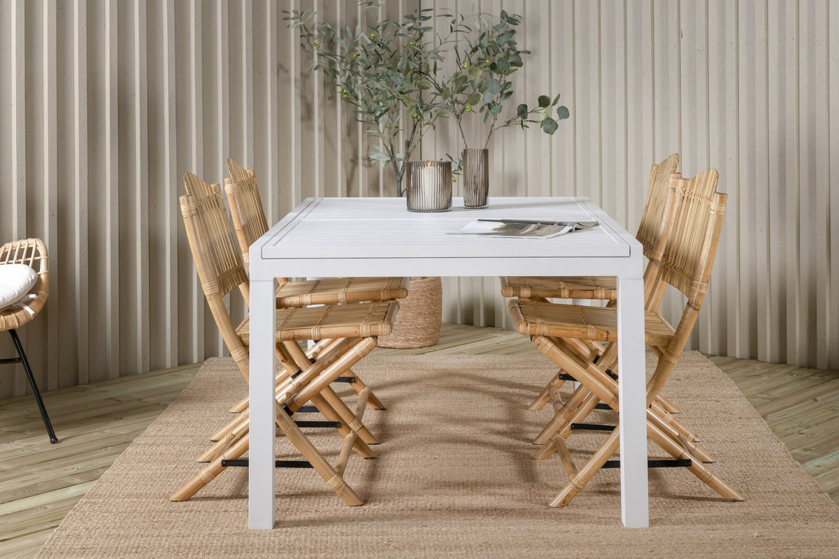 Aluminium-Caféstuhl in Natur mit Baumwoll-Polyester-Bezug neben rechteckigem Esstisch mit weisser Aluminium-Tischplatte und Rattanbeinen.
