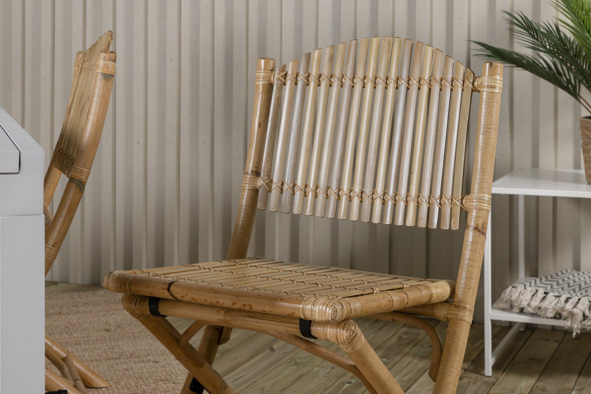 Aluminium-Caféstuhl in Natur mit Baumwoll-Polyester-Bezug neben rechteckigem Esstisch mit weisser Aluminium-Tischplatte und Rattanbeinen.