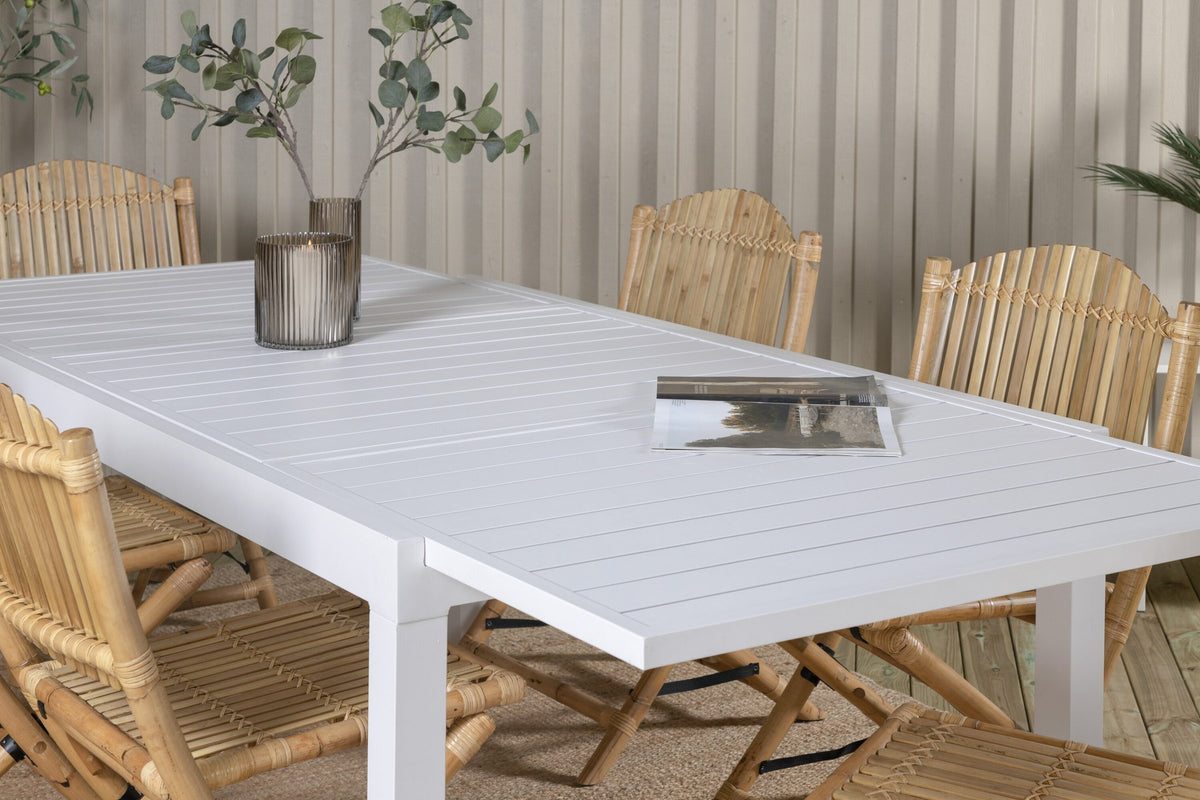Aluminium-Caféstuhl in Natur mit Baumwoll-Polyester-Bezug neben rechteckigem Esstisch mit weisser Aluminium-Tischplatte und Rattanbeinen.
