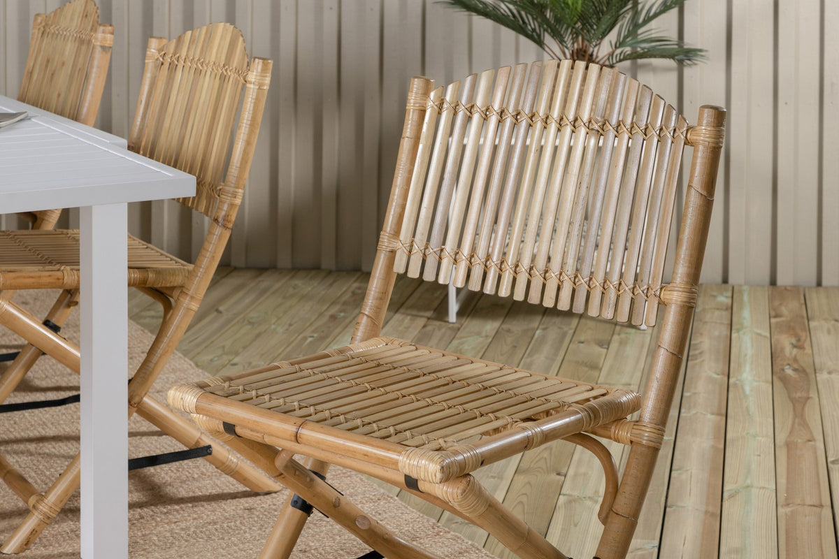 Aluminium-Caféstuhl in Natur mit Baumwoll-Polyester-Bezug neben rechteckigem Esstisch mit weisser Aluminium-Tischplatte und Rattanbeinen.