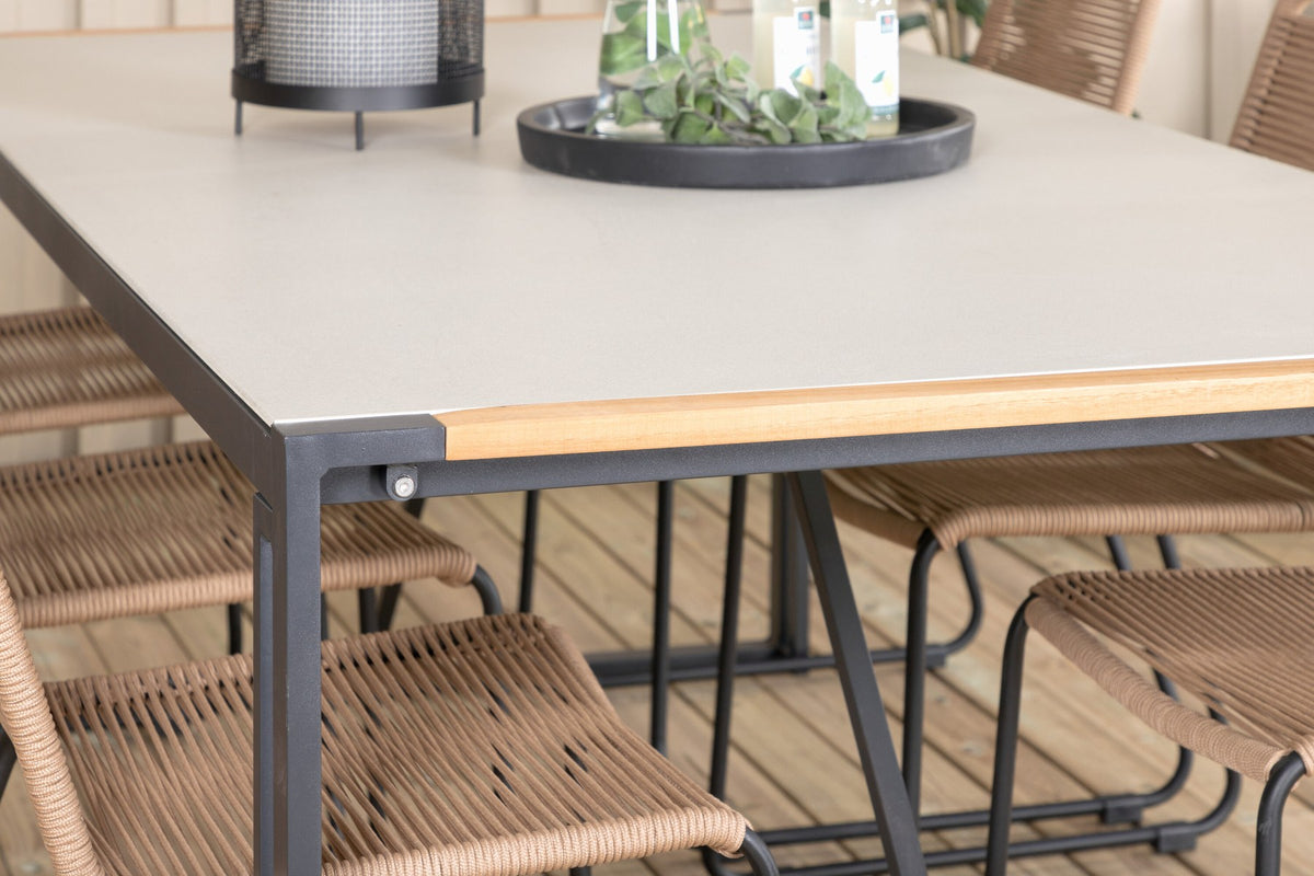 Zwei braune Esszimmerstühle mit Teakholz und Aluminium neben einem rechteckigen Glastisch mit schwarzer Tischplatte und Stahlbeinen im Aussenbereich.