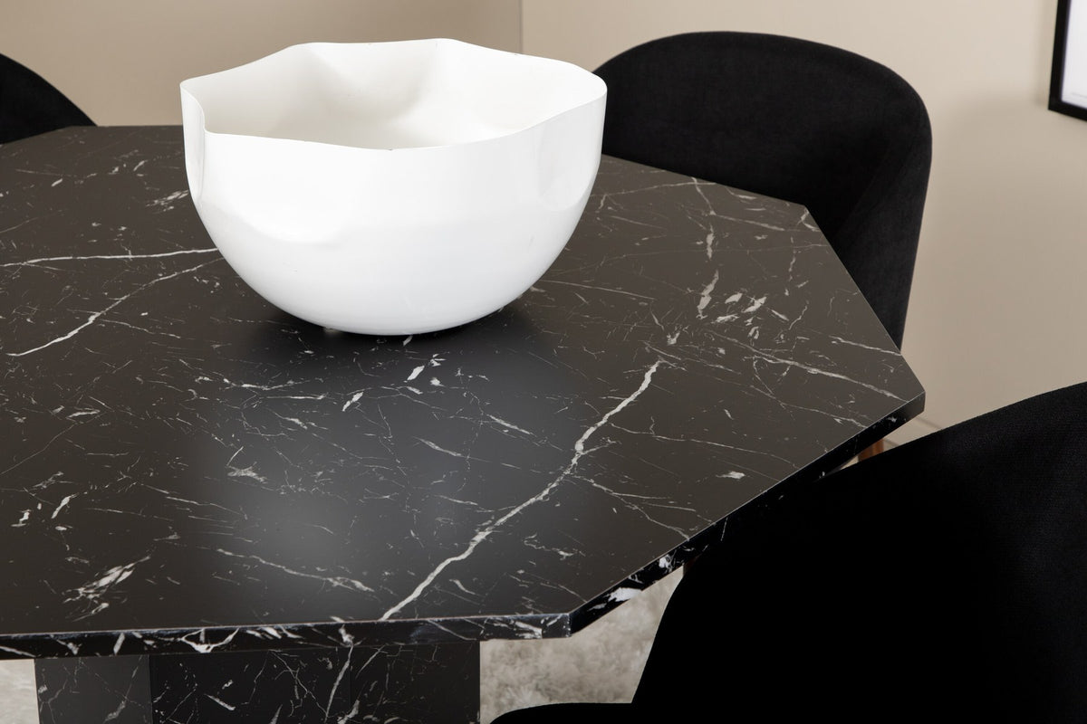 Zwei schwarze Esszimmerstühle mit Nussbaum-Beinen und Polyester-Sitzfläche neben rundem Esstisch Ø110cm mit schwarzer MDF-Platte und Stahlbeinen.