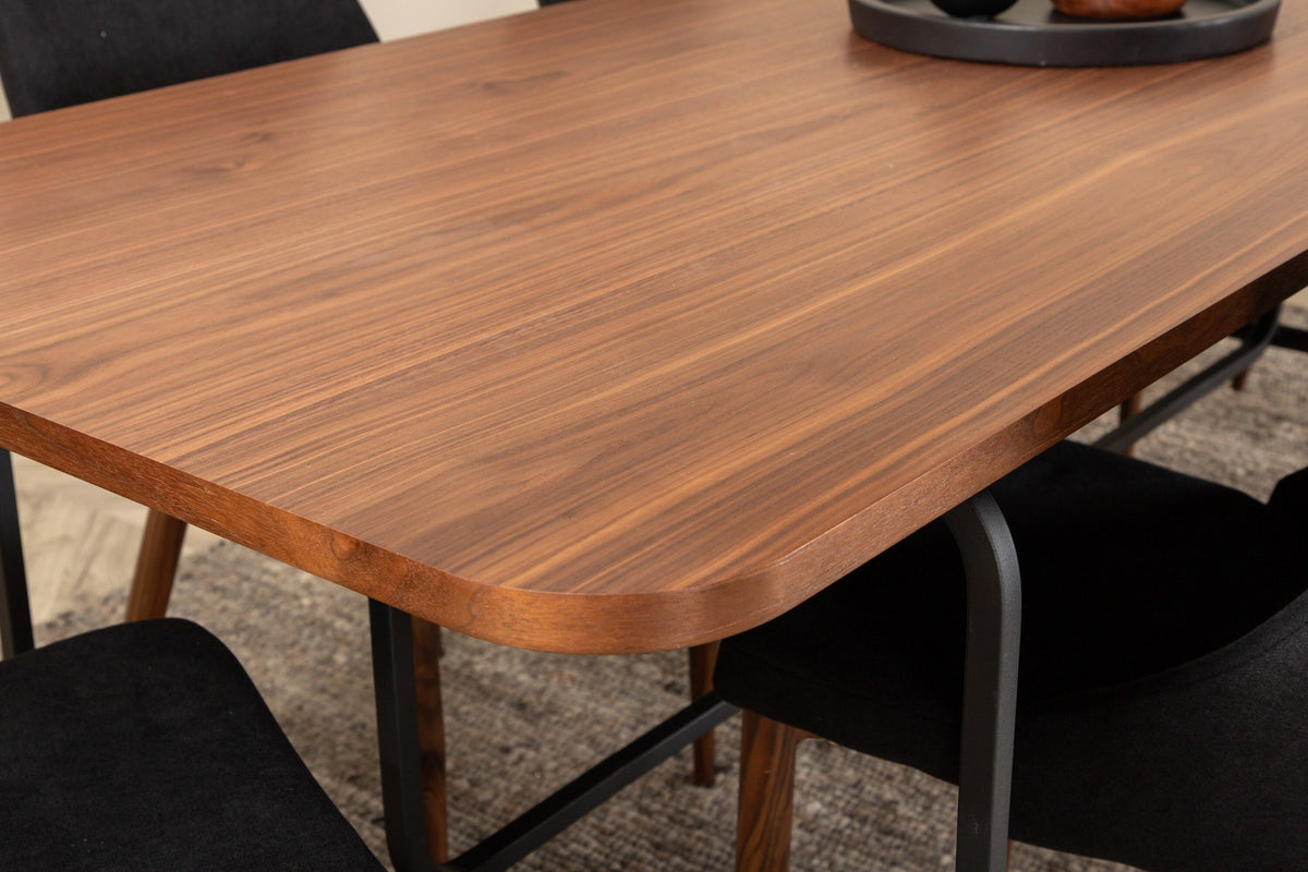 Rechteckiger Esstisch mit MDF-Tischplatte in Nussbaumfurnier und schwarzem Stahlgestell, kombiniert mit zwei schwarzen Polyester-Stühlen.