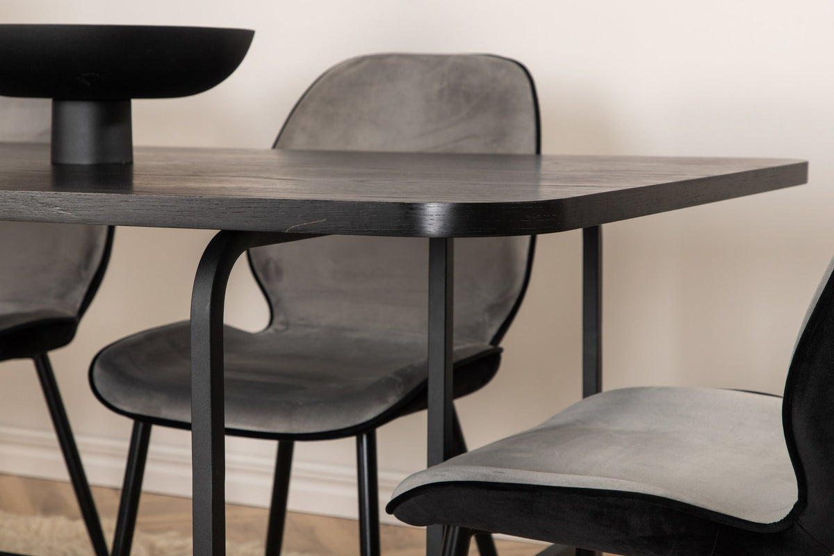 Zwei graue Esszimmerstühle mit Samtbezug und Eisenbeinen neben einem rechteckigen schwarzen Esstisch aus MDF mit Furnier und Metallgestell.