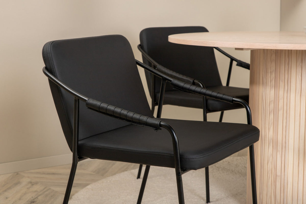 Rundes Esszimmerset aus MDF: Tischplatte Ø110 cm in Whitewash mit gerippten Beinen, dazu zwei schwarze Stühle mit Eisenbeinen.