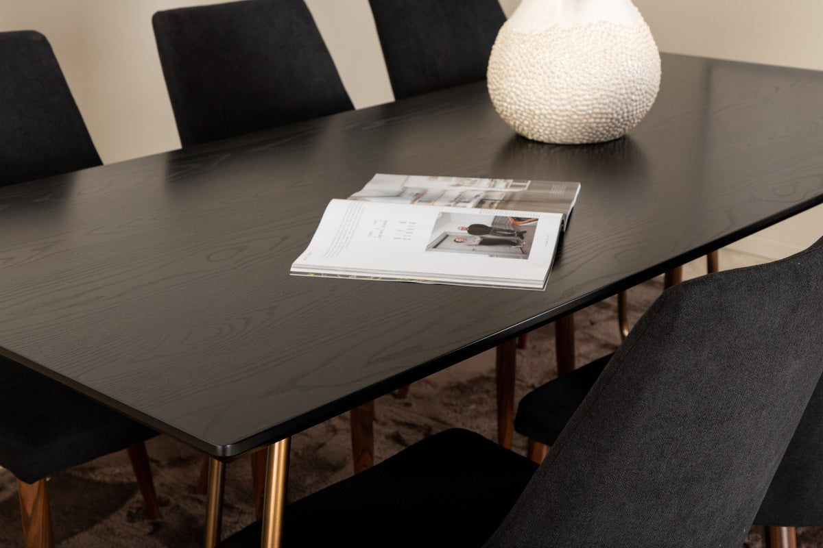 Rechteckiger Esstisch aus schwarzem MDF mit Furnier und Stahlbeinen, dazu zwei Esszimmerstühle mit schwarzer Sitzfläche und Metallgestell.