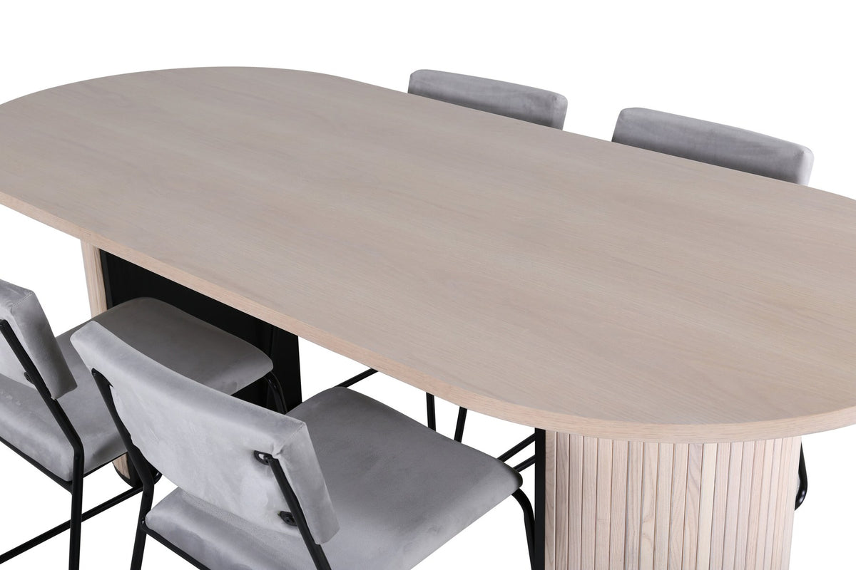 Zwei graue Esszimmerstühle mit schmalen schwarzen Beinen neben ovalem Esstisch mit MDF-Platte in Whitewash, Grösse 200x90 cm.