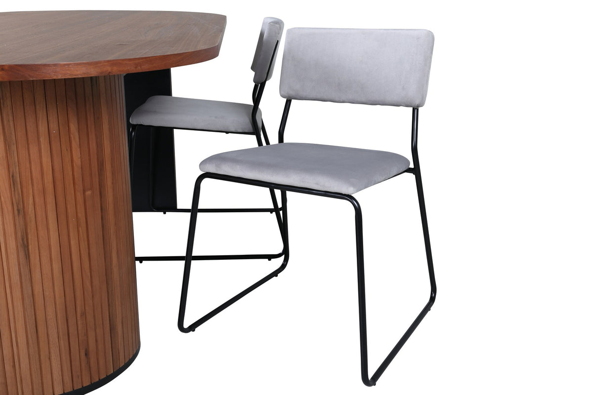 Zwei graue Esszimmerstühle mit schmalen Metallbeinen und samtigem Sitz neben ovalem Esstisch aus Nussbaum-MDF mit Furnier, 200x90cm.