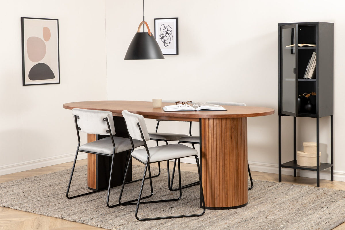 Zwei graue Esszimmerstühle mit schmalen Metallbeinen und samtigem Sitz neben ovalem Esstisch aus Nussbaum-MDF mit Furnier, 200x90cm.