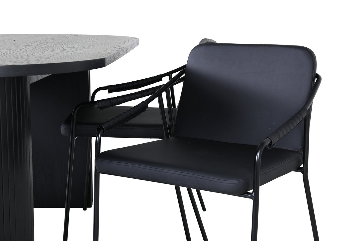Zwei schwarze Esszimmerstühle mit Beinen aus Eisen und Sitzfläche aus Polyurethan-Membran neben ovalem MDF-Esstisch in Schwarz.