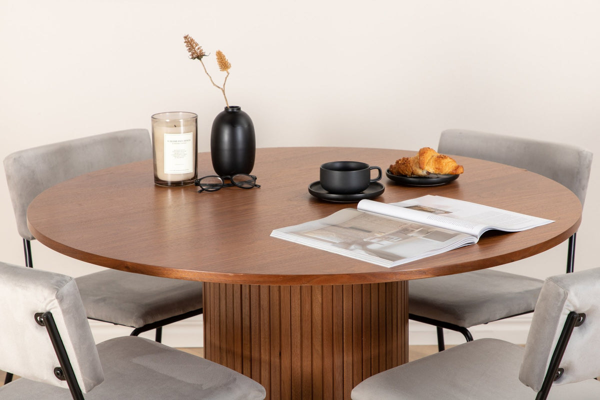 Zwei graue Esszimmerstühle mit schwarzem Metallgestell neben einem runden Esstisch aus Nussbaum-MDF mit Furnier, Durchmesser 110cm.