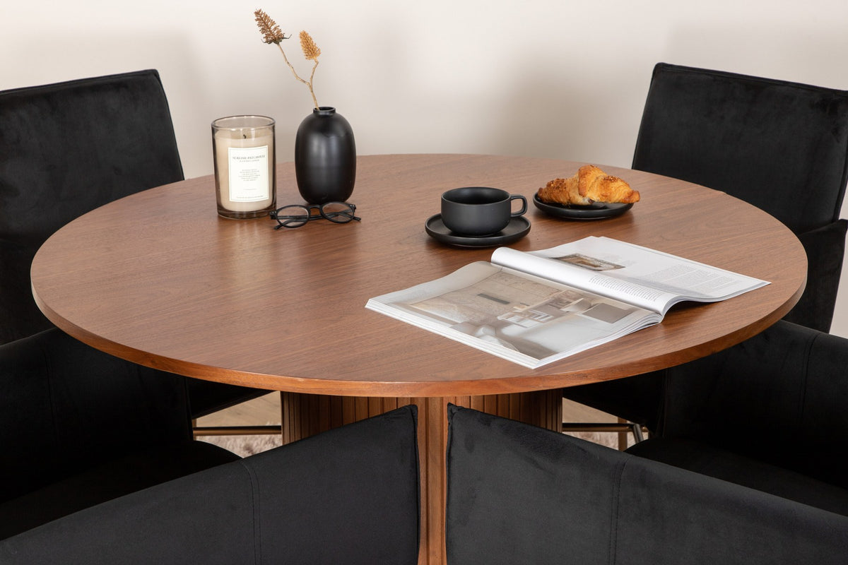 Rundes Esszimmerset mit Nussbaum-Tischplatte Ø110cm aus MDF und vier schwarzen Stühlen mit Samtsitz und Beinen aus Eisen.