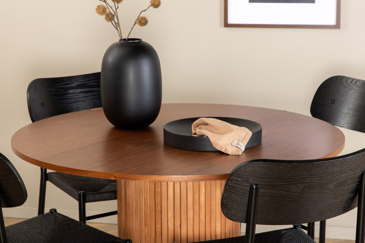 Rundes Esszimmerset Bianca mit Stuhl Polly: Tisch aus MDF und Furnier in Walnuss, vier schwarze Stühle mit Metallbeinen und Seilsitzen.