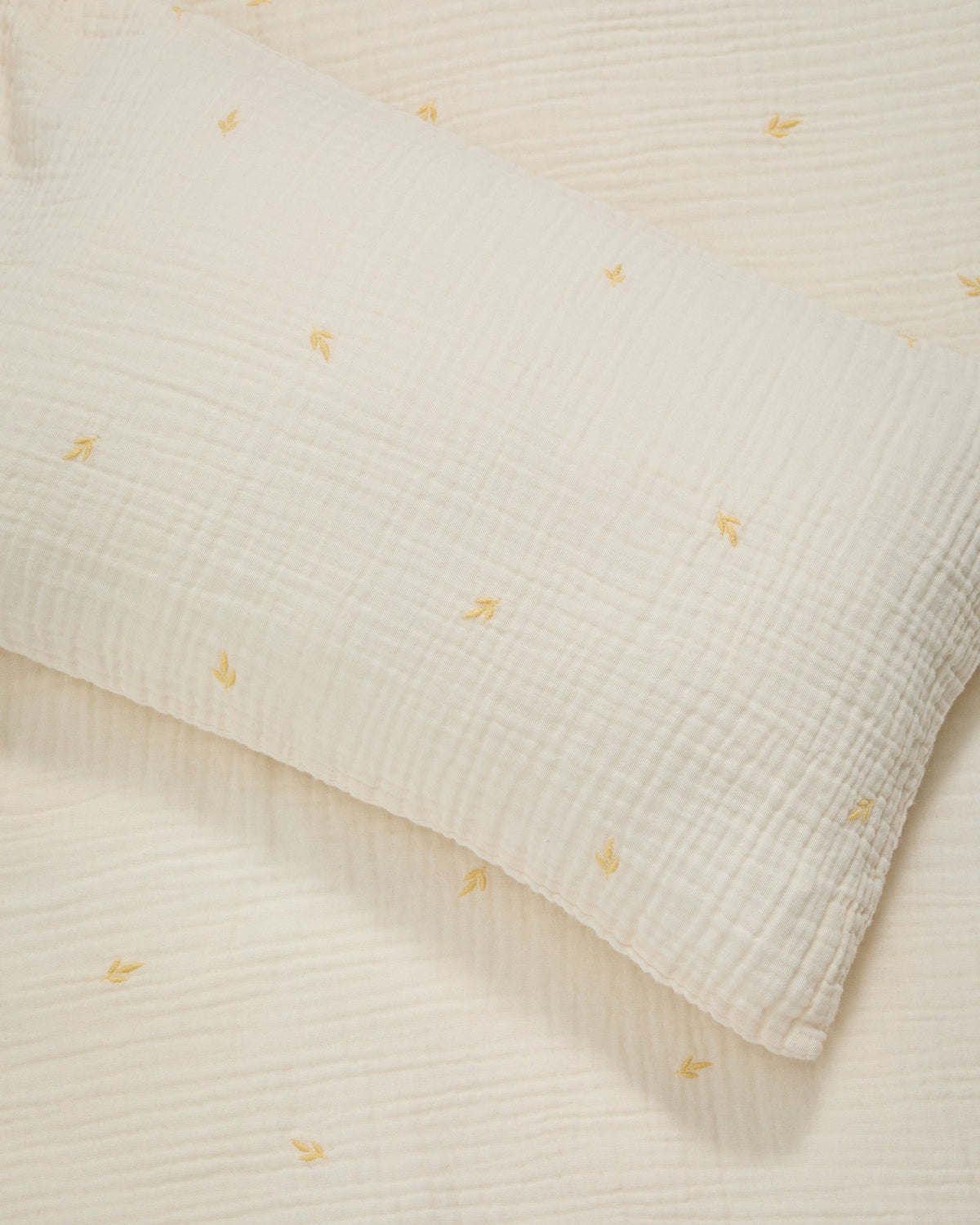 Bettbezug und Kopfkissen aus ecrufarbener Baumwoll-Doppelgaze mit aufgestickten Blättern, für Babybett, Set Dorani von Kave Home.