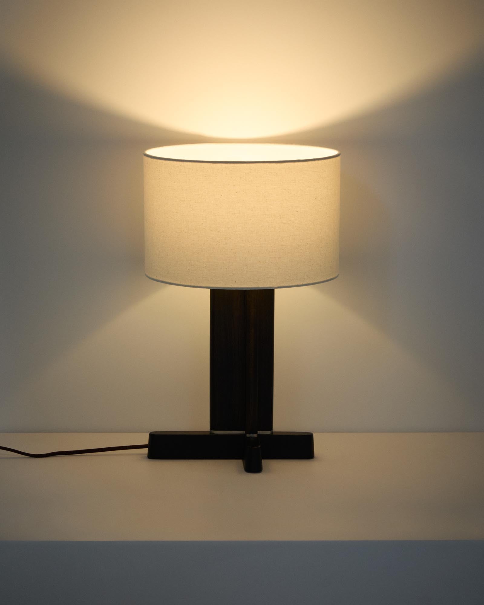Elegante Tischleuchte Niani aus Kautschukholz mit dunkler Oberfläche und einem 30 cm großen elfenbeinfarbenen Baumwollschirm, ideal für stimmungsvolle Beleuchtung.