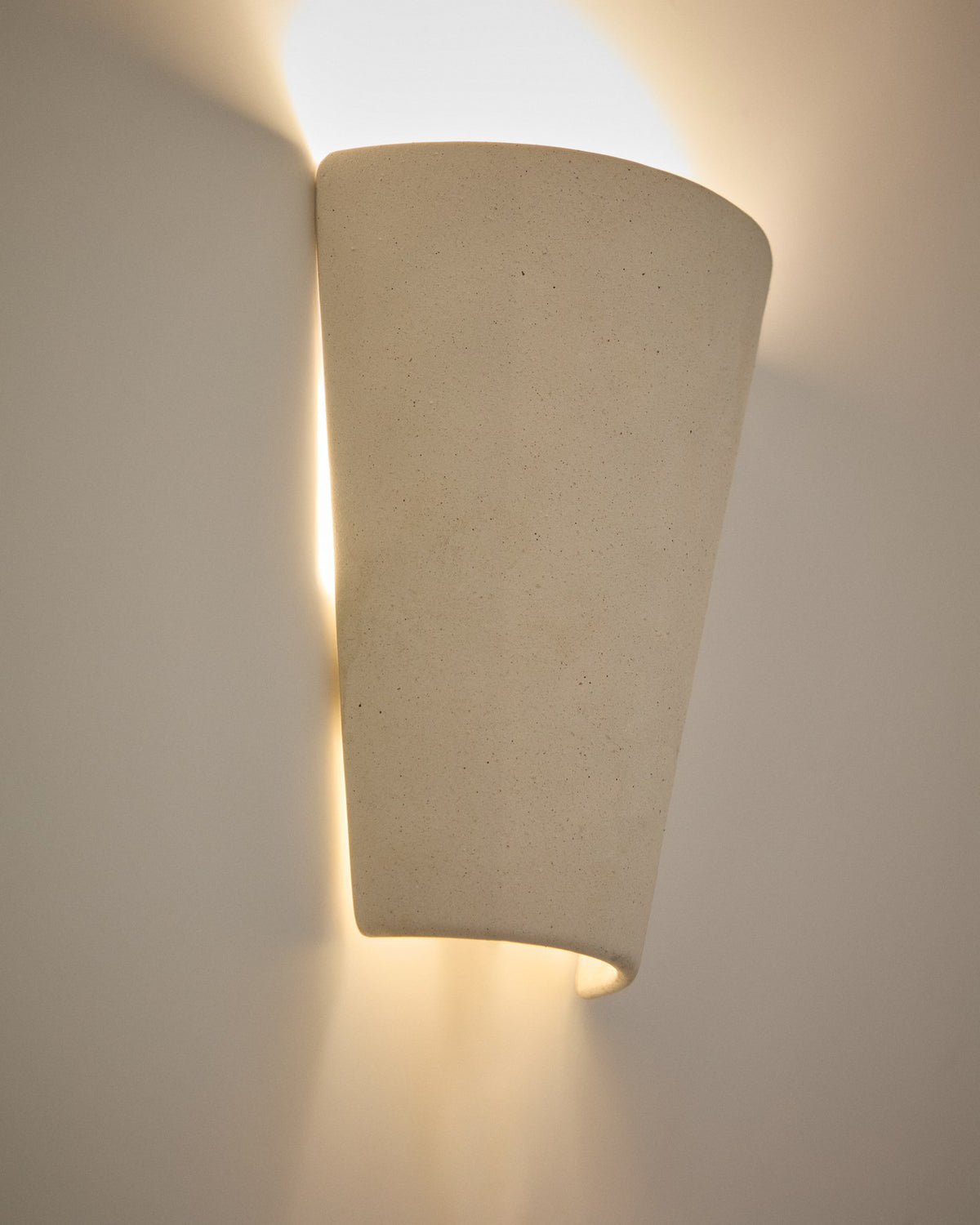 Wandleuchte Ceren aus weisser Keramik mit klaren Formen und runder Silhouette, montiert an einer hellen Wand, Grösse 12x6x14 cm.