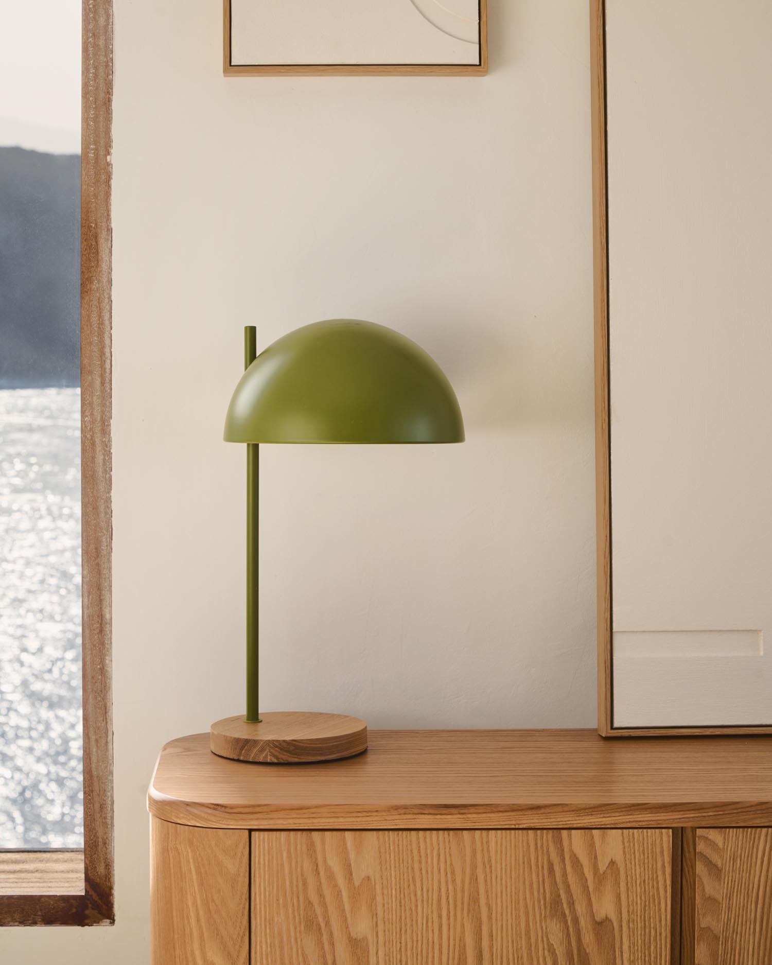 Die Catlar Tischlampe von Kave Home kombiniert elegantes Eschenholz mit einem frischen grünen Metallfinish und passt perfekt in jedes moderne Zuhause.